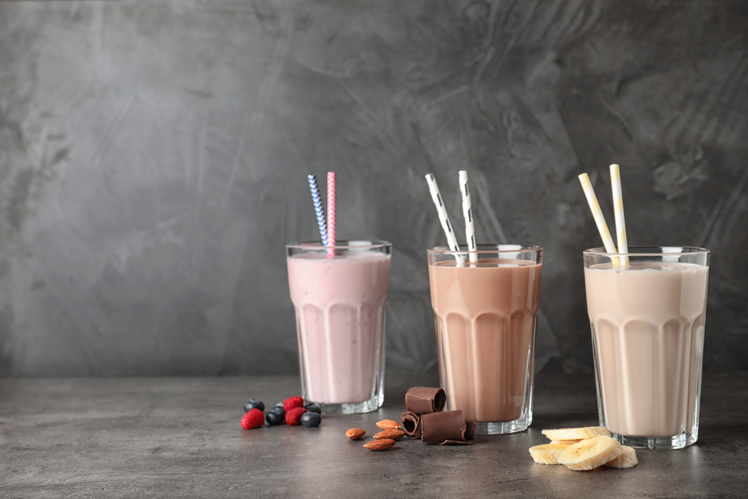 Glasses with different protein shakes and ingredients on table against grey background. Space for text